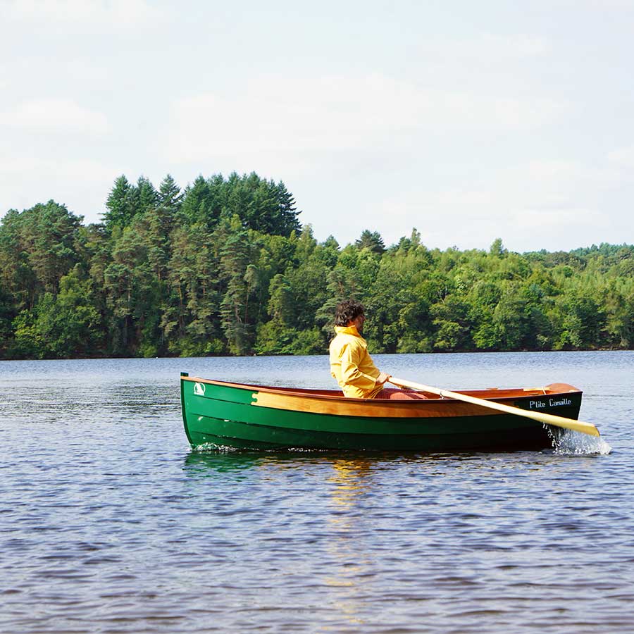 Bateau en bois vert P’tite Canaille naviguant sur un lac entouré d’arbres