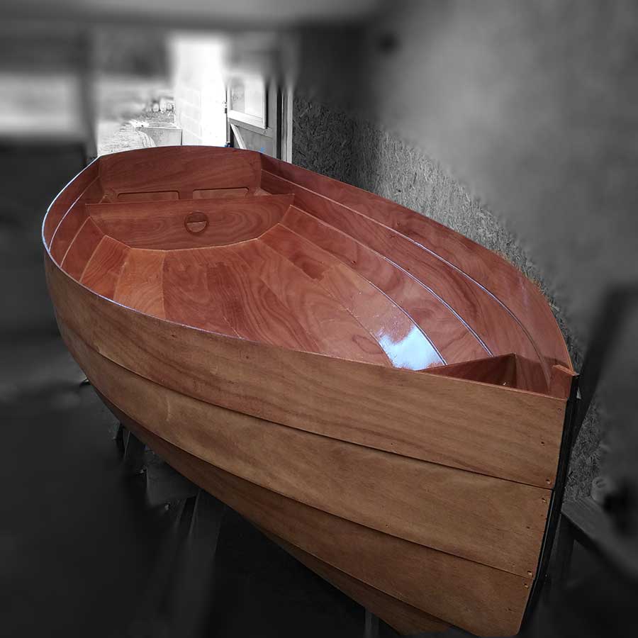 Coque en bois verni du voilier P’tite Canaille en cours de construction dans un atelier.