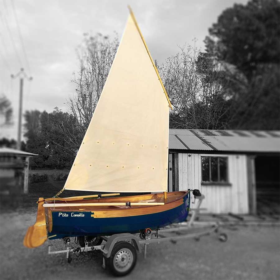 Voilier en bois bleu P’tite Canaille sur sa remorque devant un atelier