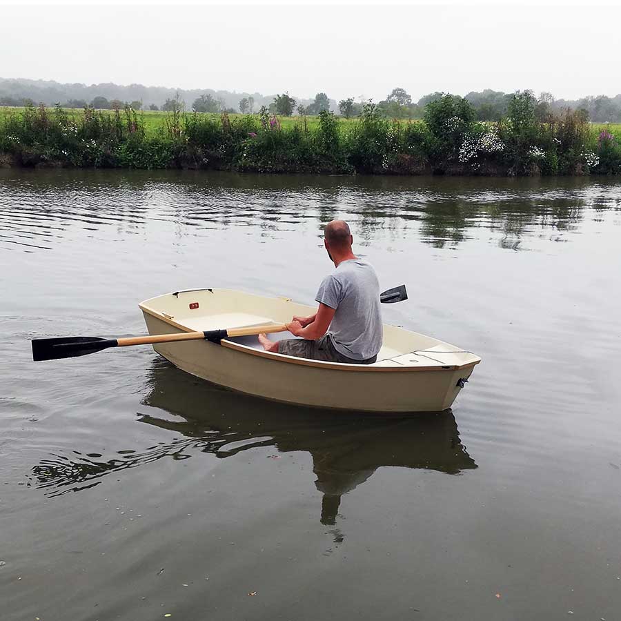 Homme ramant seul à bord d’un petit bateau en bois Sardinette sur une rivière paisible.